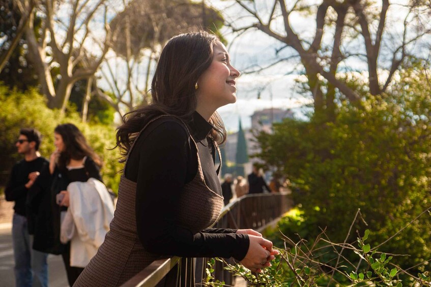 A person leaning on a railing, overlooking a park with trees and a distant building. 1