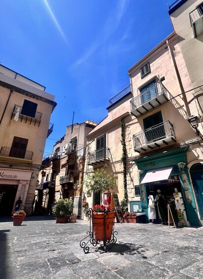 A sunny street with buildings, a potted plant, and a shop entrance. 2