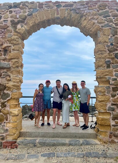 A group of people standing under a stone archway with a view of the sea. 5