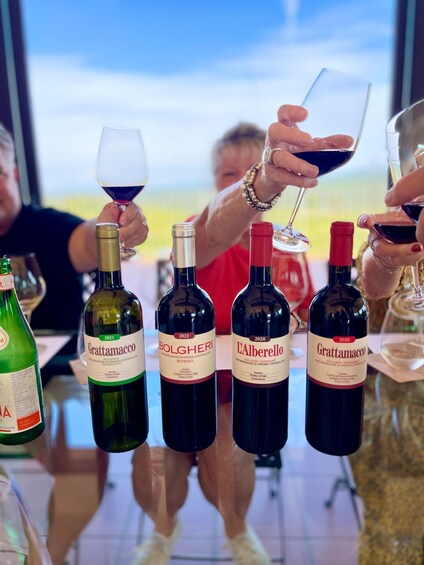 A group of people toasting with wine glasses, with bottles of Grattamacco wine in front of them. 2