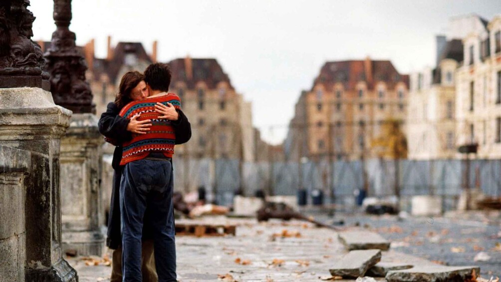 A couple embracing on a stone pathway with buildings in the background. 1
