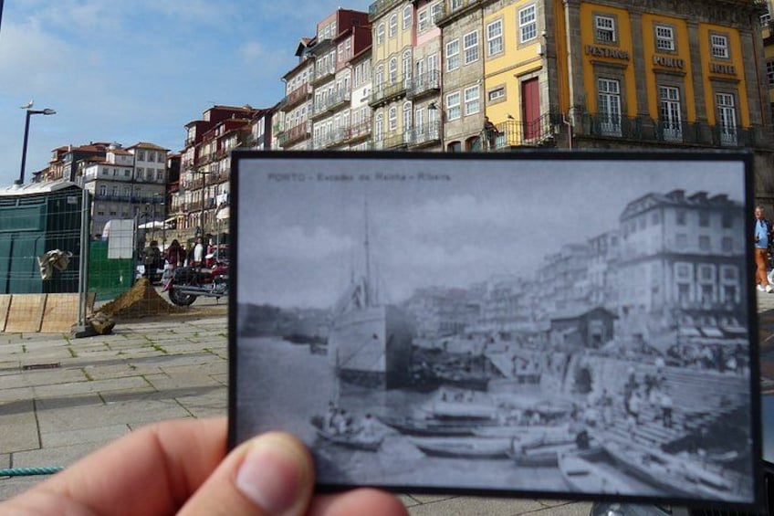A hand holding a photograph of a historic street scene with buildings and boats. 1