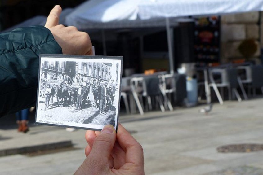 A person holding a black and white photo of a street scene with buildings and people. 5