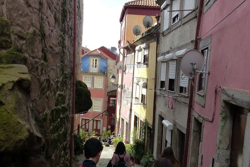 A narrow alley with colorful buildings, a stone wall, and a staircase. 2