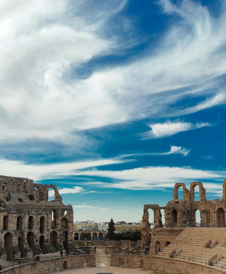 Ancient ruins with arches and columns, set against a backdrop of a clear blue sky with scattered clouds. 3