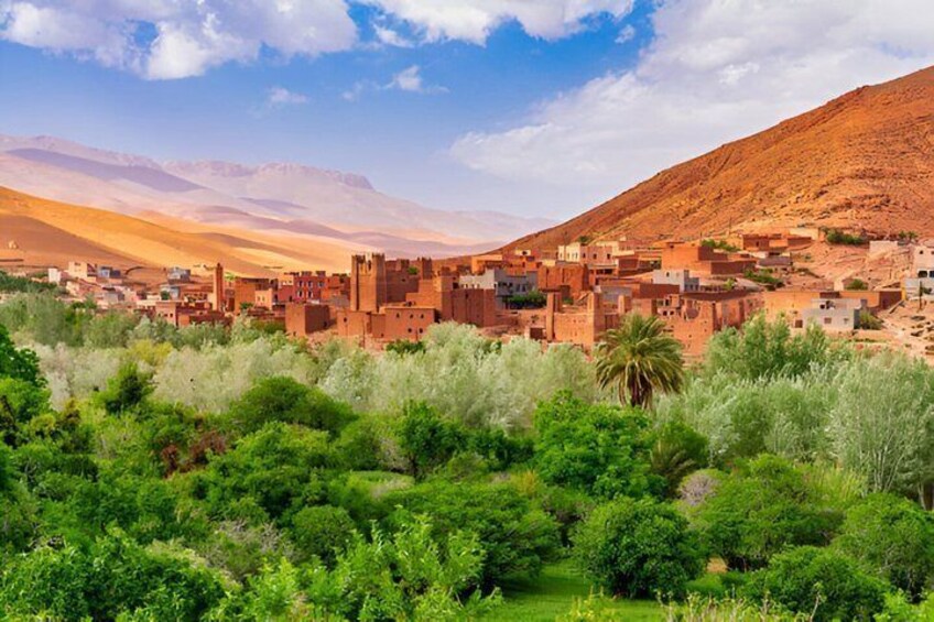 A desert town with traditional buildings, green vegetation, and mountains in the background. 3