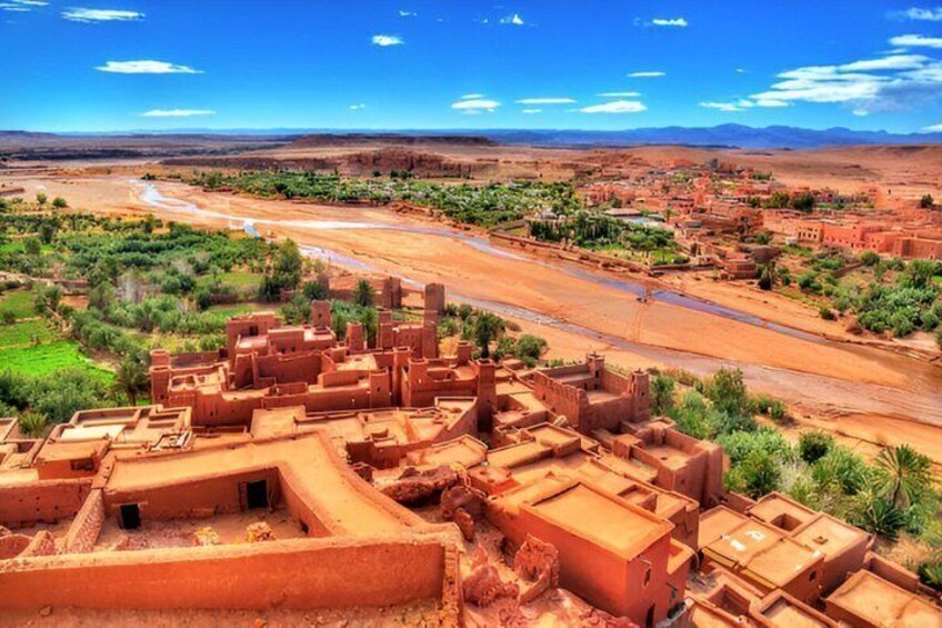A desert landscape with a river, traditional mud-brick buildings, and distant mountains. 2