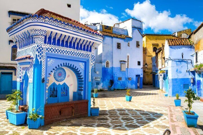 A blue and white building with intricate patterns, a cobblestone street, and potted plants. 4