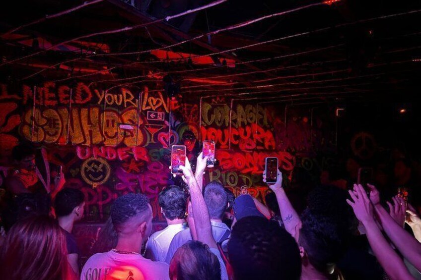 A crowd at an indoor event with graffiti-covered walls and people holding up smartphones. 4