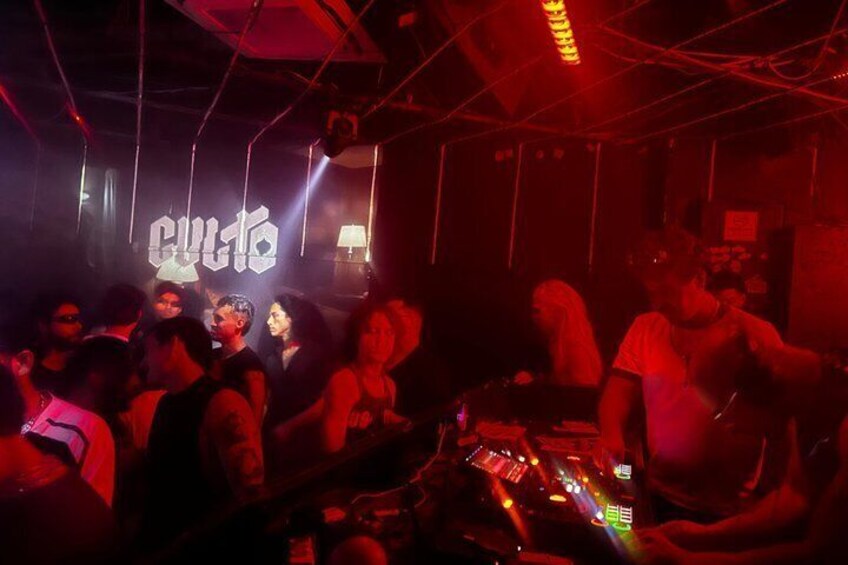 A crowded club with a DJ booth and a neon sign. 3