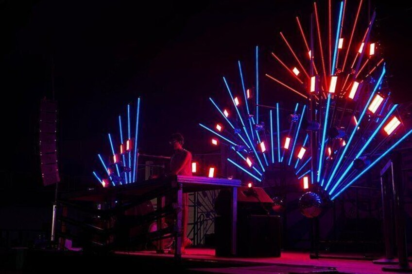 A person playing a keyboard on a stage with a backdrop of blue and red neon lights. 1