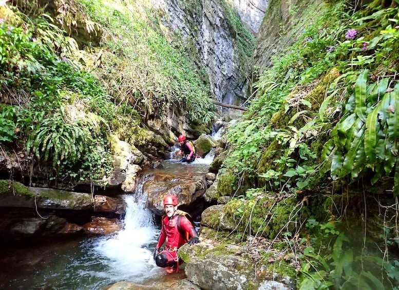 A person in red gear wading through a stream in a rocky, forested area. 4