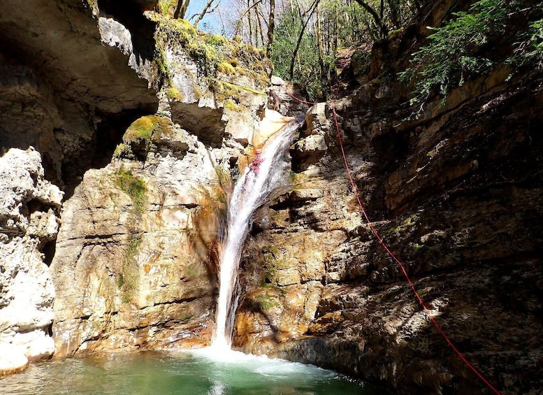 A waterfall cascading into a pool surrounded by rocky cliffs and greenery. 2
