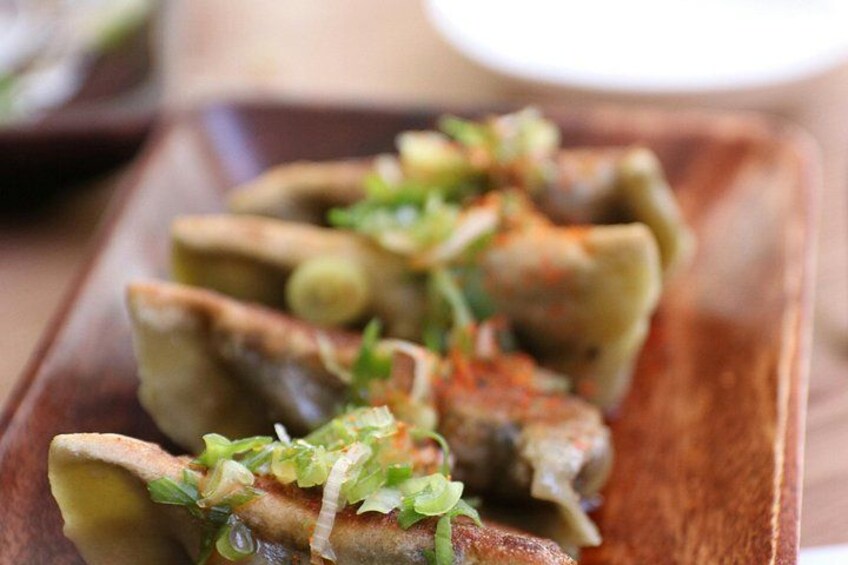 A wooden board with several pieces of food, possibly dumplings, garnished with green herbs and a red spice. 2