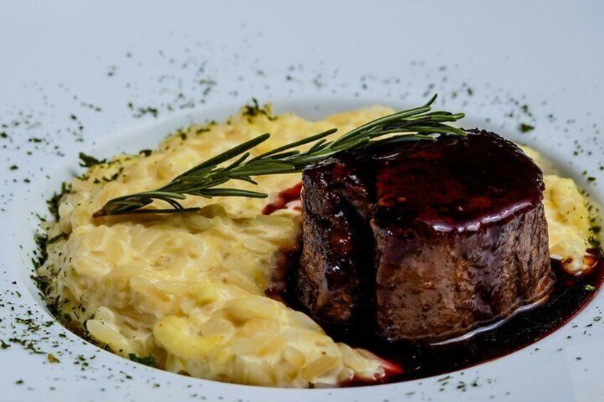 A steak with a dark sauce and a sprig of rosemary on a plate with mashed potatoes. 1