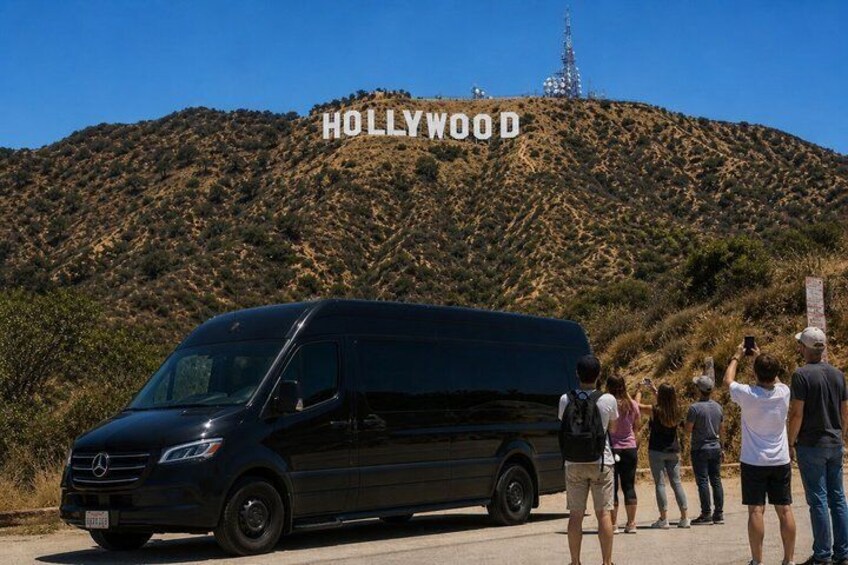 A black van parked in front of the Hollywood sign with people standing behind it. 2