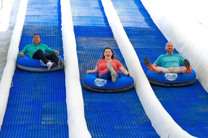Three people sliding down a blue inflatable tube slide. 2