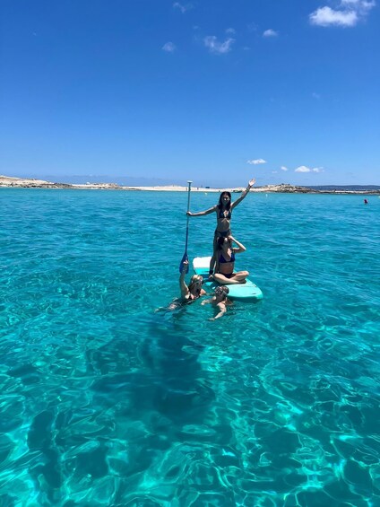Two people in a clear blue sea, one standing on a surfboard and the other paddling. 2