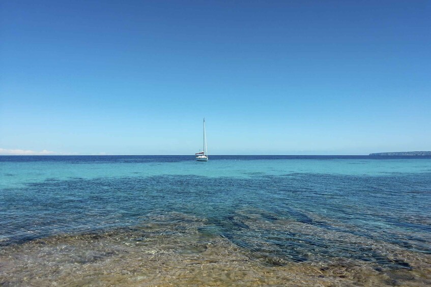 A clear blue sea with a sailboat anchored in the distance. 3