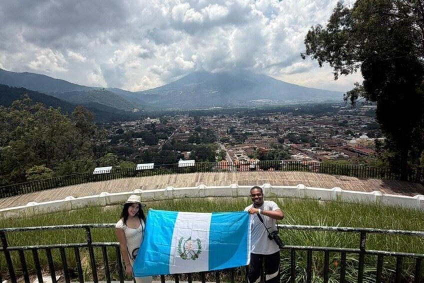 A person holding a flag, a railing, and a mountainous landscape in the background. 3