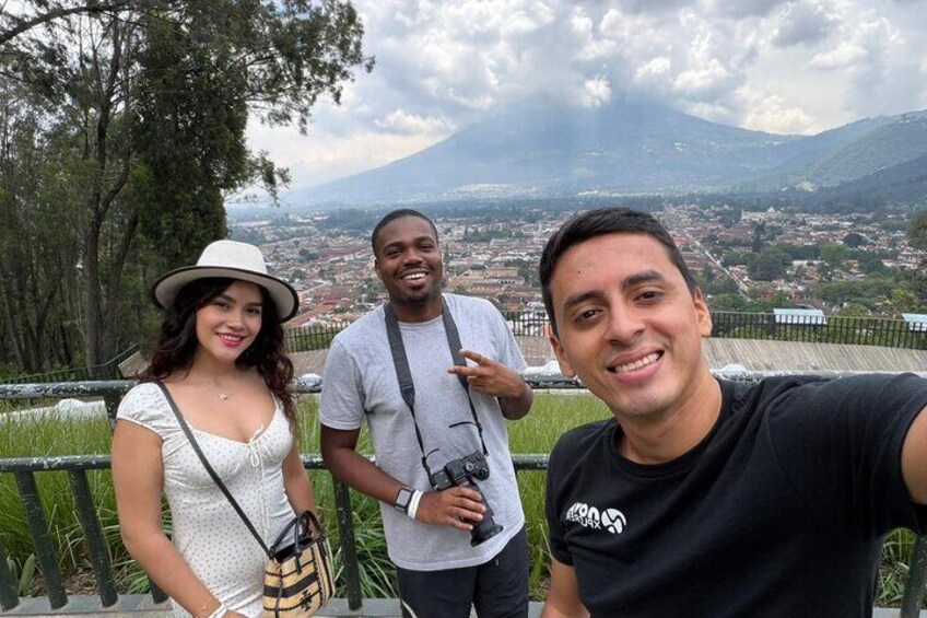 Three people standing on a viewing platform with a city and mountains in the background. 2