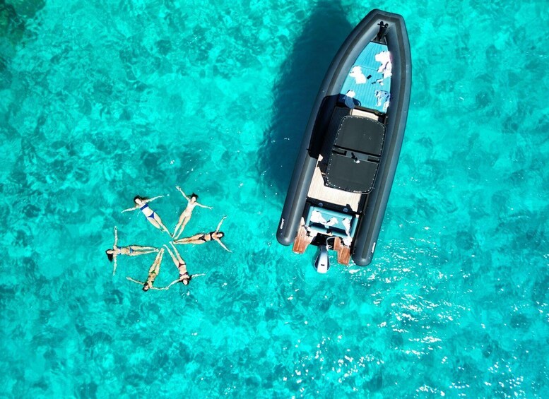 A small inflatable boat on turquoise water with people swimming around it. 1