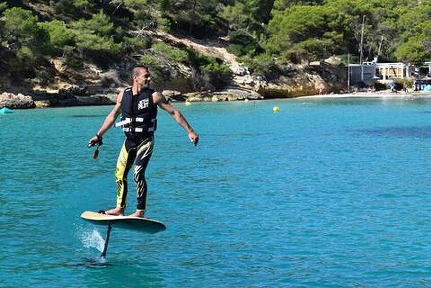 A person stand-up paddleboarding on clear blue water with a rocky shoreline and greenery in the background. 4