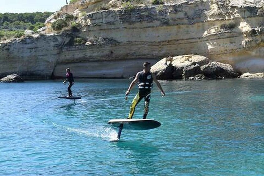 Two people surfing on a calm sea with cliffs in the background. 2