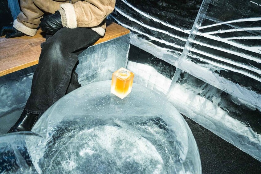 A person sitting next to a large ice sculpture with a yellow cube in the center. 3