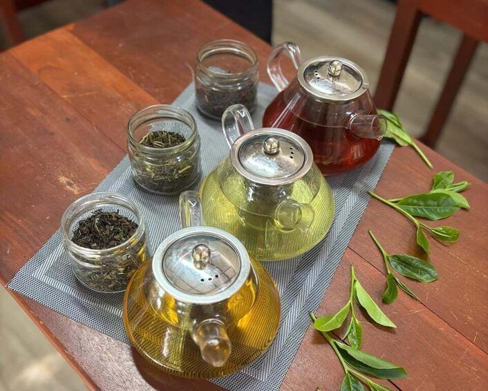 A wooden table with tea-making equipment, including a teapot, a glass jar, and loose tea leaves. 4