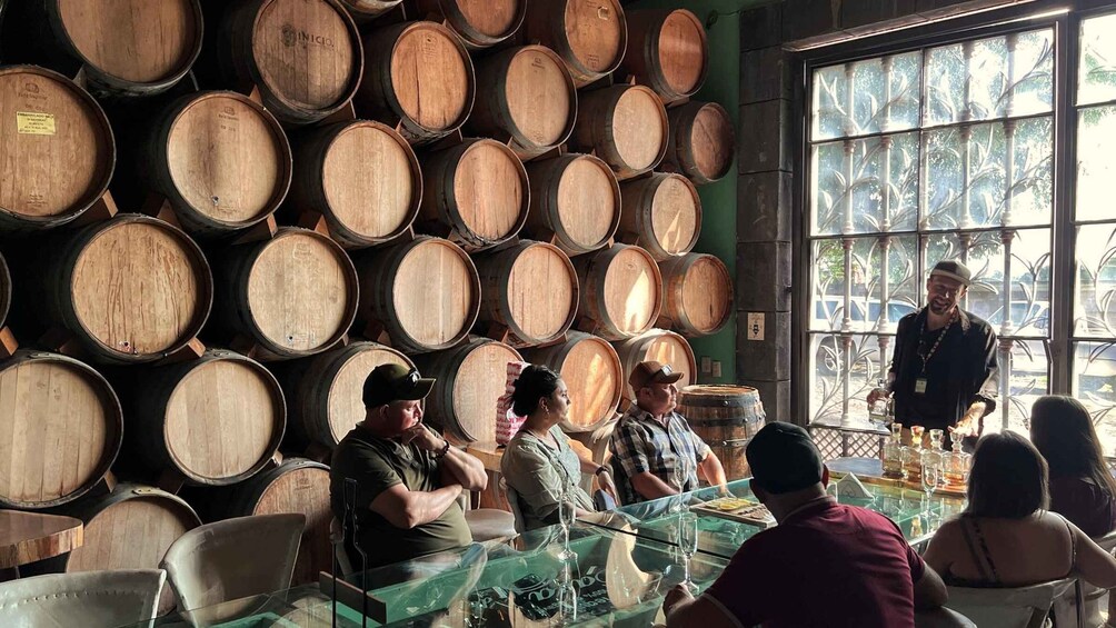 A group of people seated at a table inside a room with wooden barrels stacked against the wall. 3