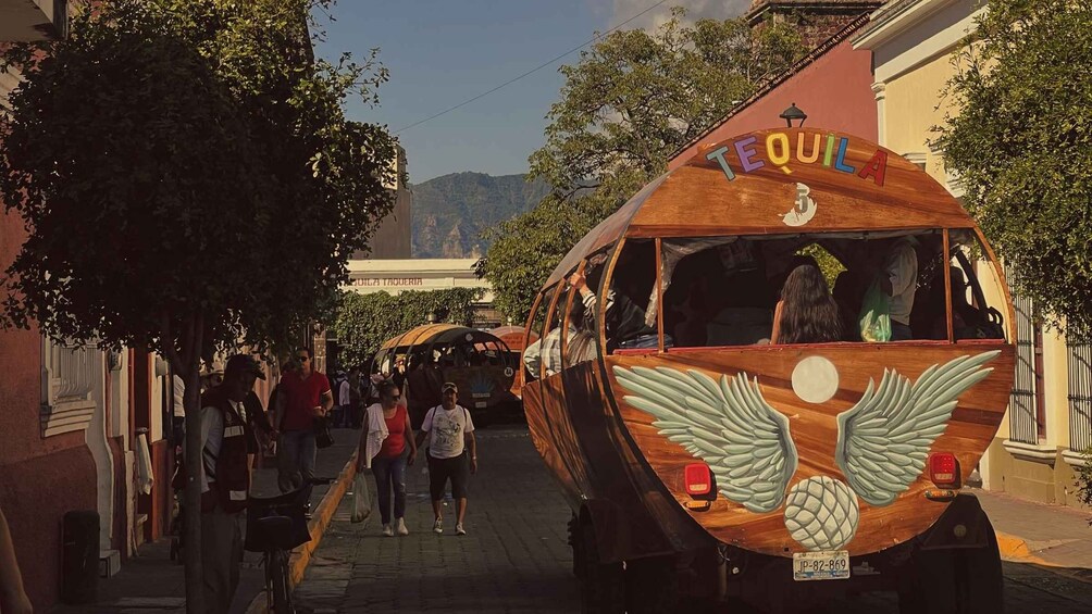A wooden vehicle with 'TEQUILA' and a bird logo, parked on a street with pedestrians. 4
