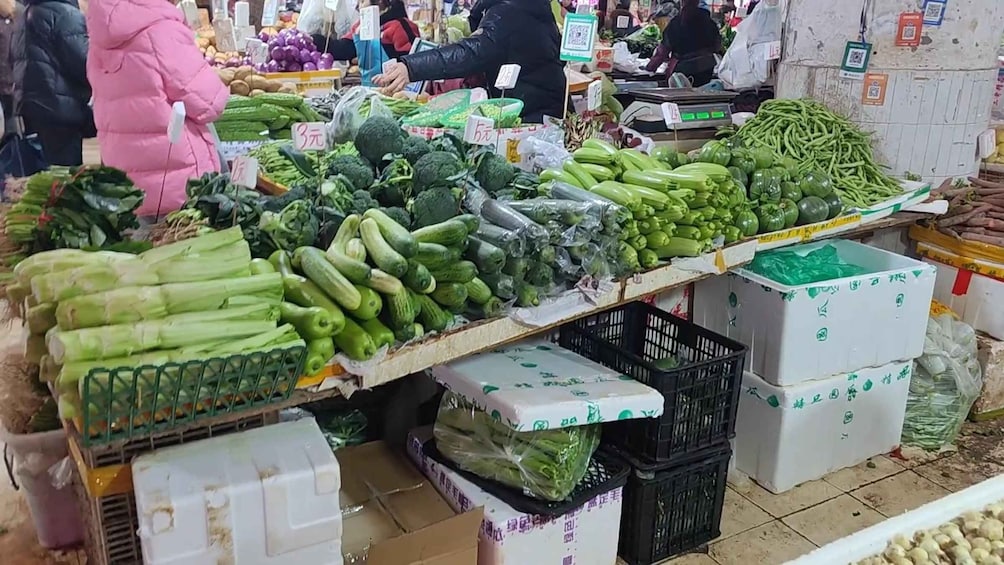 A vegetable market with various fresh produce on display, including cucumbers, broccoli, and green beans. 3