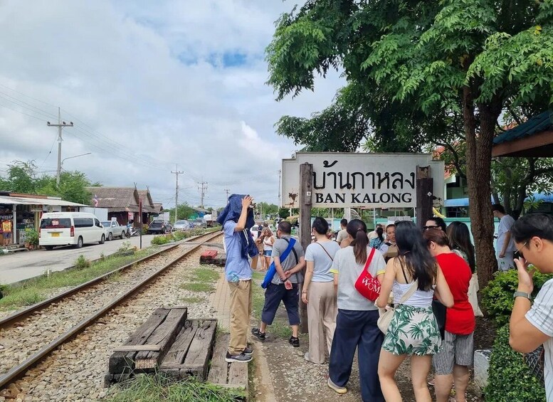 A group of people standing by a railway track with a sign reading 'BAN KALONG'. 3