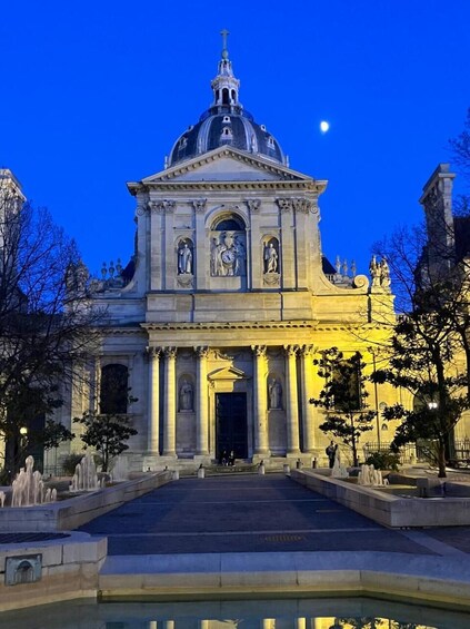 A grand building with a dome and statues, surrounded by a reflective pool and trees. 5