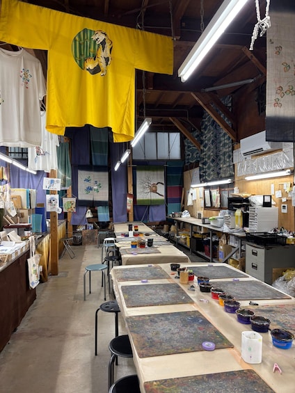 An art studio with tables covered in paint, art supplies, and hanging artwork. 4