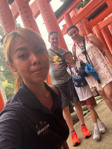 A group of people standing in front of red torii gates with Japanese writing. 2