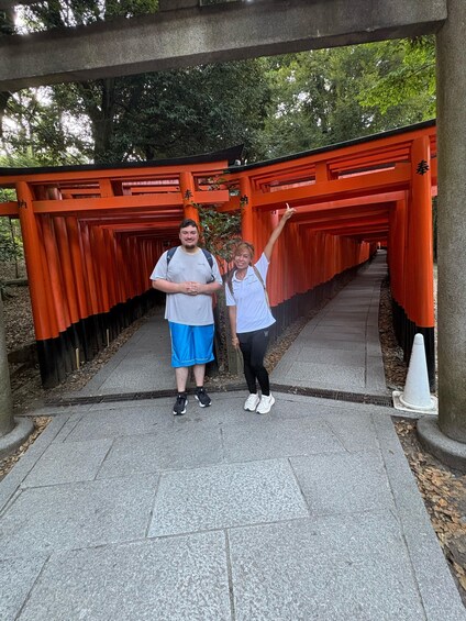 Two people standing under a red torii gate with a pathway leading through it. 3