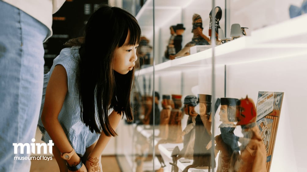 A person examining a display of vintage toys and puppets in a museum. 1