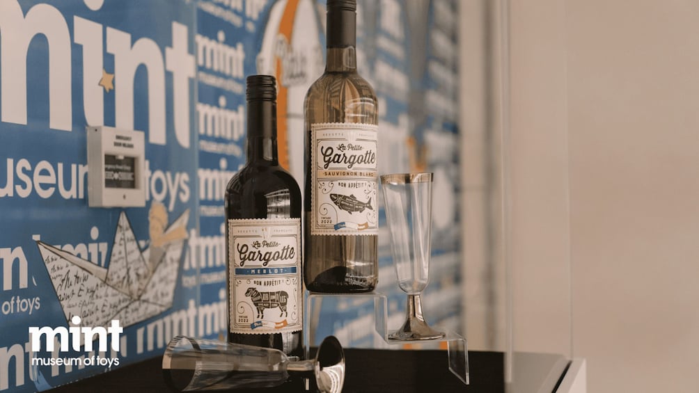 Two bottles of La Petite Gargotte wine and a glass on a table with a background of a blue wall with white text and a toy sailboat. 4