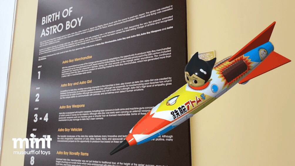 A toy rocket with a character on it, placed on a display board with text about the 'Birth of Astro Boy.' 5