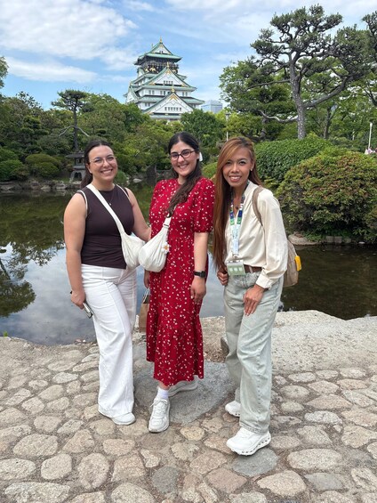 Three people standing by a pond with a traditional Japanese building in the background. 3