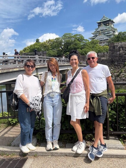 A group of people standing in front of a historic castle with a bridge in the background. 5