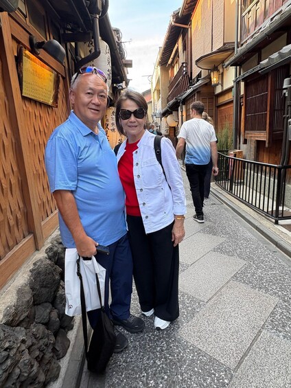 A narrow street with wooden buildings, a stone wall, and a metal fence. 4