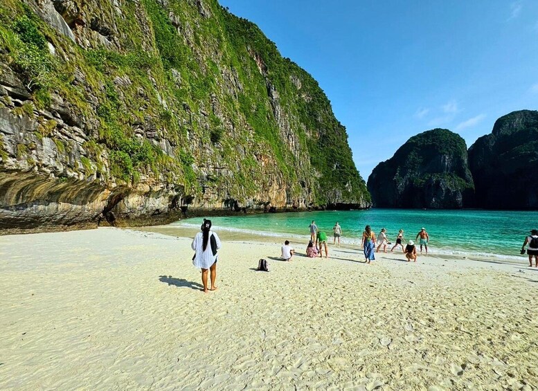 A beach with clear turquoise water, sandy shore, and lush green cliffs. 4