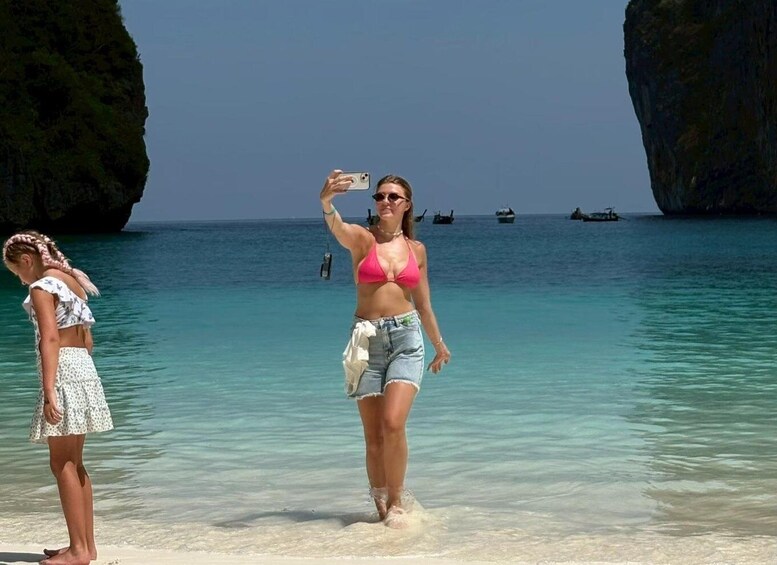 Two people taking a selfie on a beach with clear turquoise water and large rock formations in the background. 5