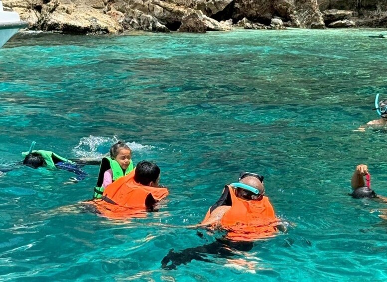 People snorkeling in clear turquoise water with rocky cliffs in the background. 2