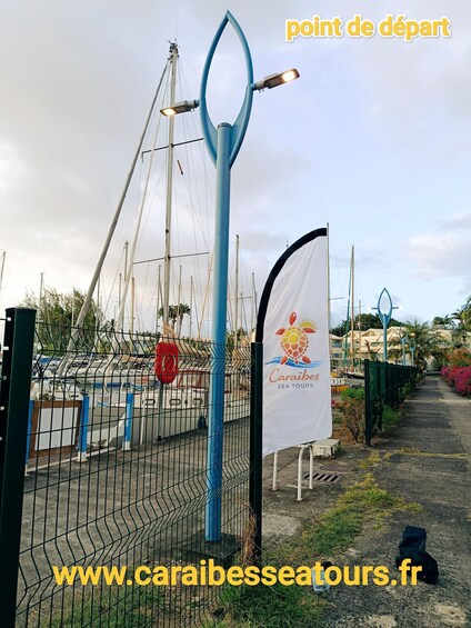A marina with boats, a blue flagpole, and a sign for Caraibes Sea Tours. 4