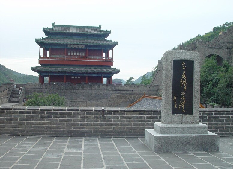 A traditional Chinese building with a multi-tiered roof, a stone monument with inscriptions, and a stone wall with steps leading up to the building. 3