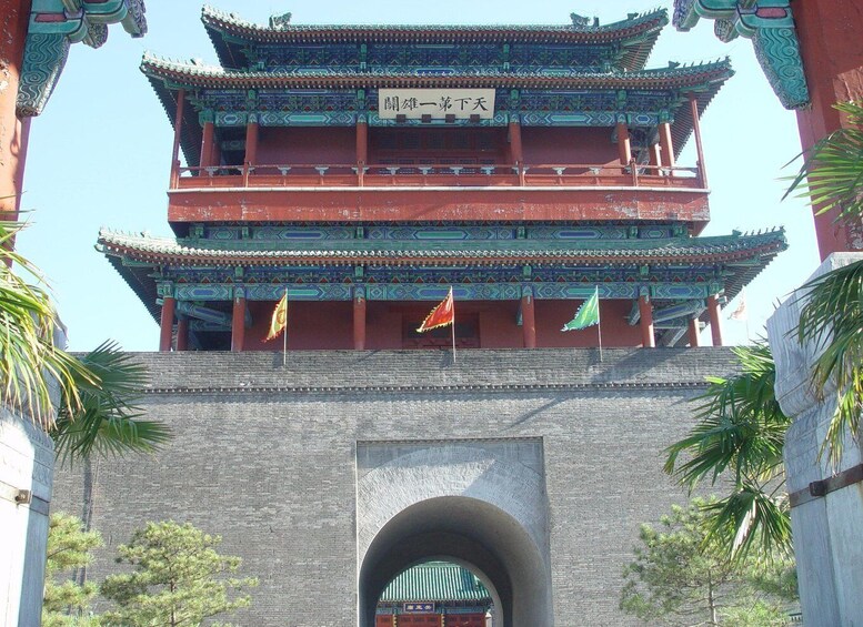 A traditional multi-tiered gate with flags, surrounded by stone walls and palm trees. 1